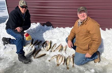 Two men are kneeling in the snow next to a pile of fish.