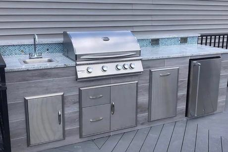 A stainless steel outdoor kitchen with a grill , sink and refrigerator.