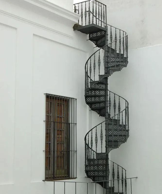Black spiral staircase outside a white building, next to a barred window.
