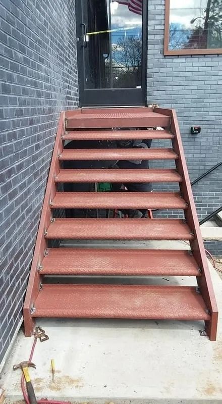 Brown metal exterior staircase leading to a black door, attached to a brick building.