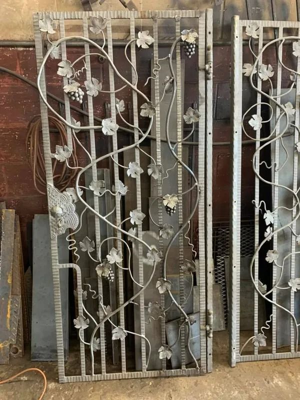 Two metal gates with vine and grape details; industrial setting.