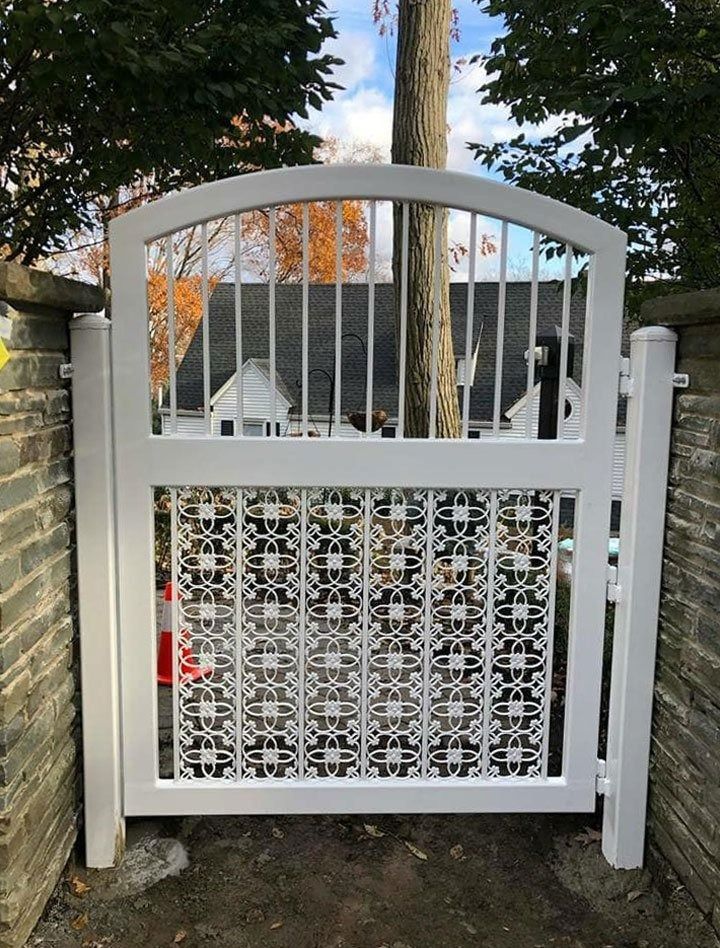 White metal gate with decorative lower panel, arched top, set between stone columns.