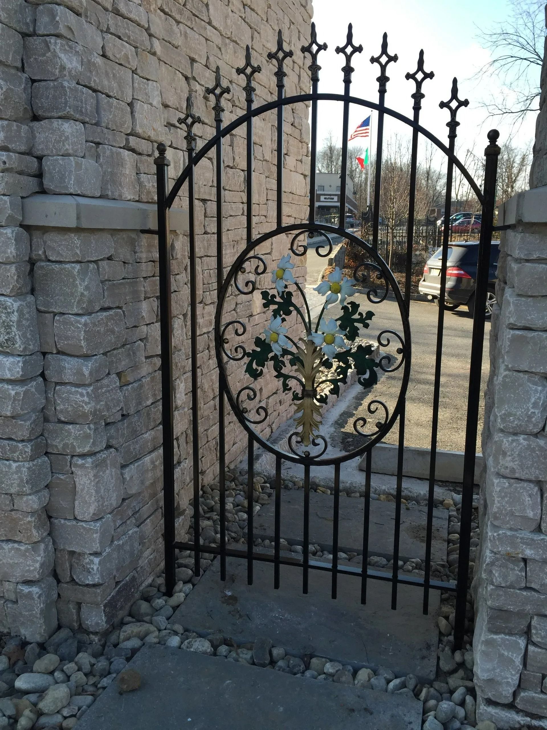 Black wrought iron gate set in a stone wall, with decorative floral design in the center.