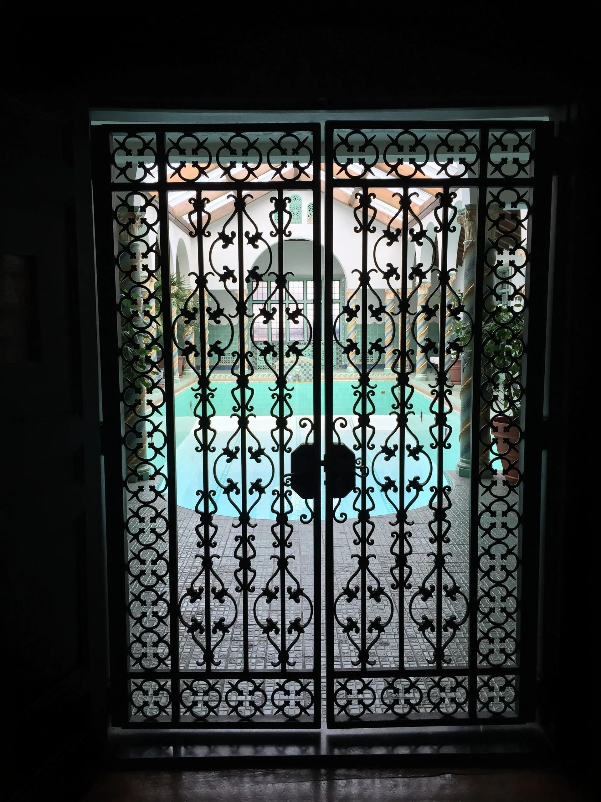 Ornate wrought iron doors open to a courtyard with a blue pool.