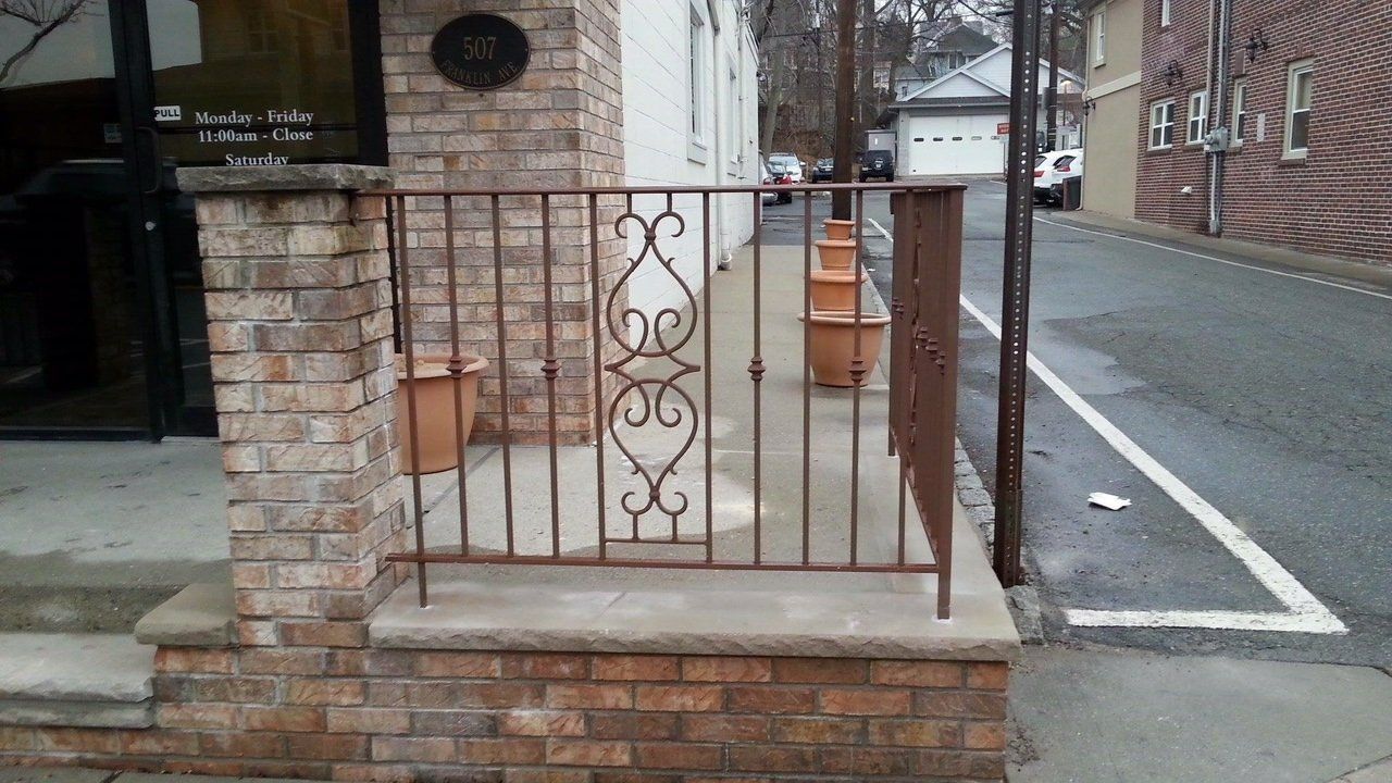 Brick building entrance with a wrought iron railing, pots, and a street view.