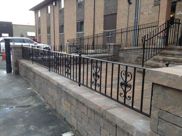 Black metal railing atop a stone wall, leading to building entrance.