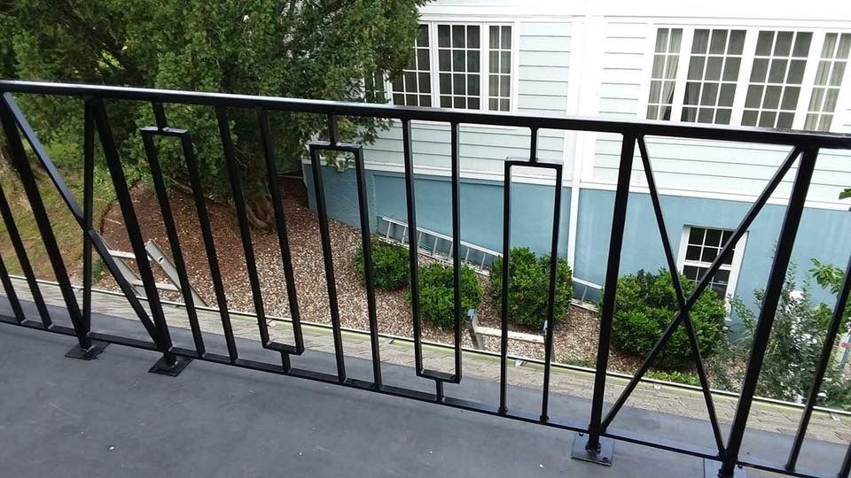 Black metal railing on a gray surface with a light blue building and green bushes in the background.