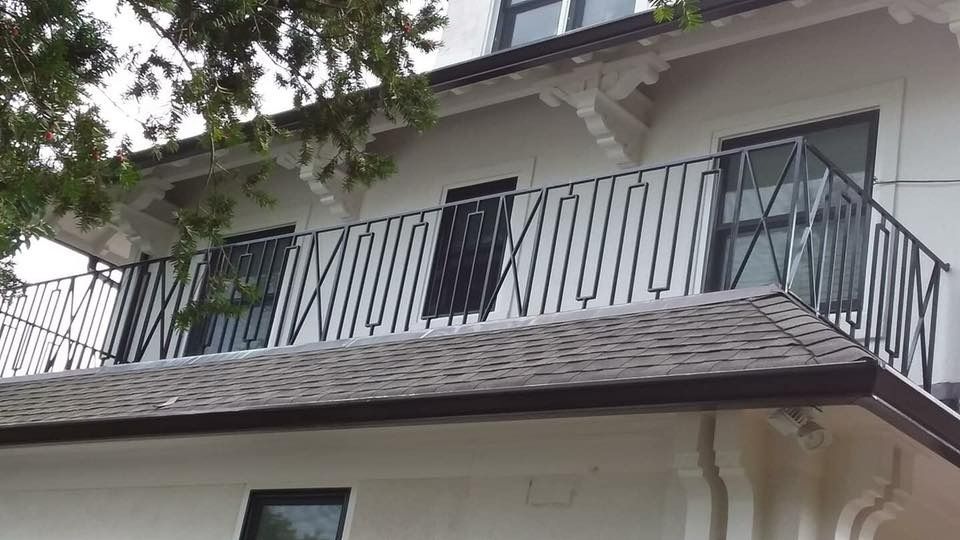 Balcony with black metal railing on a white building, dark windows.