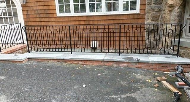 Black wrought iron fence on a gray stone wall in front of a wood-sided building.