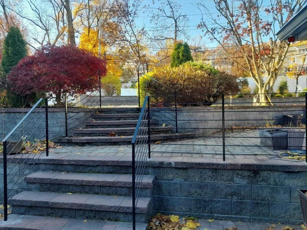 Brick steps leading up to a patio with a black railing, colorful fall trees in background.