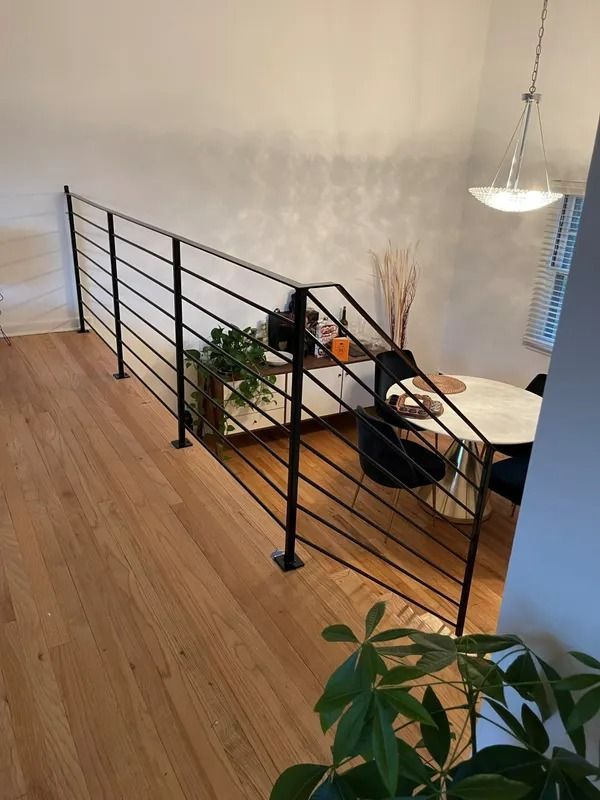 Black metal railing along a wooden floor overlooking a dining area with a round table.