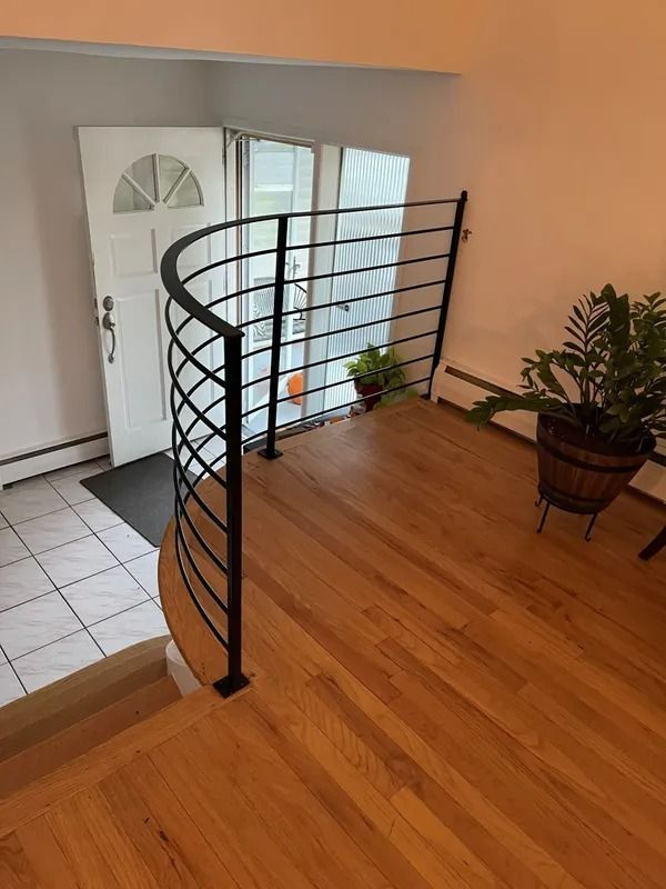 Black metal curved railing on a wood floor landing by a white front door.