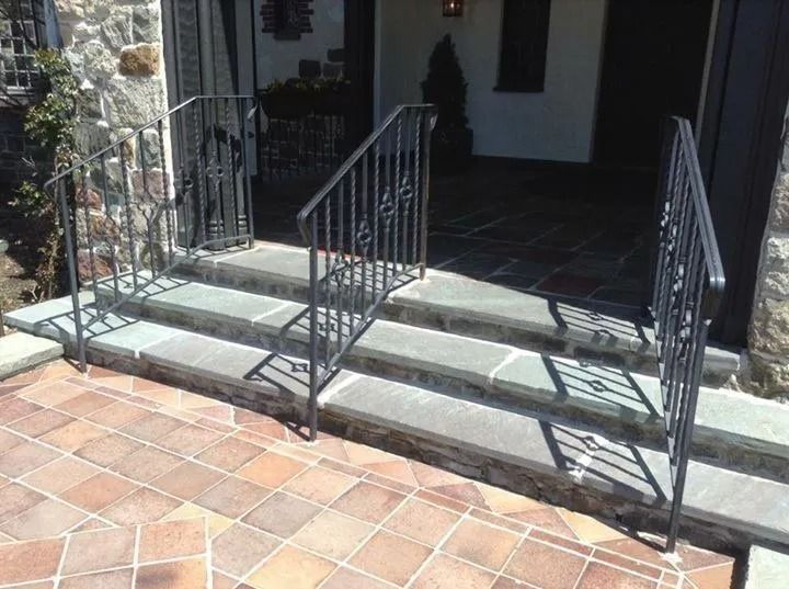 Stone steps with black iron railings leading to a doorway. Brick pavers cover the foreground.