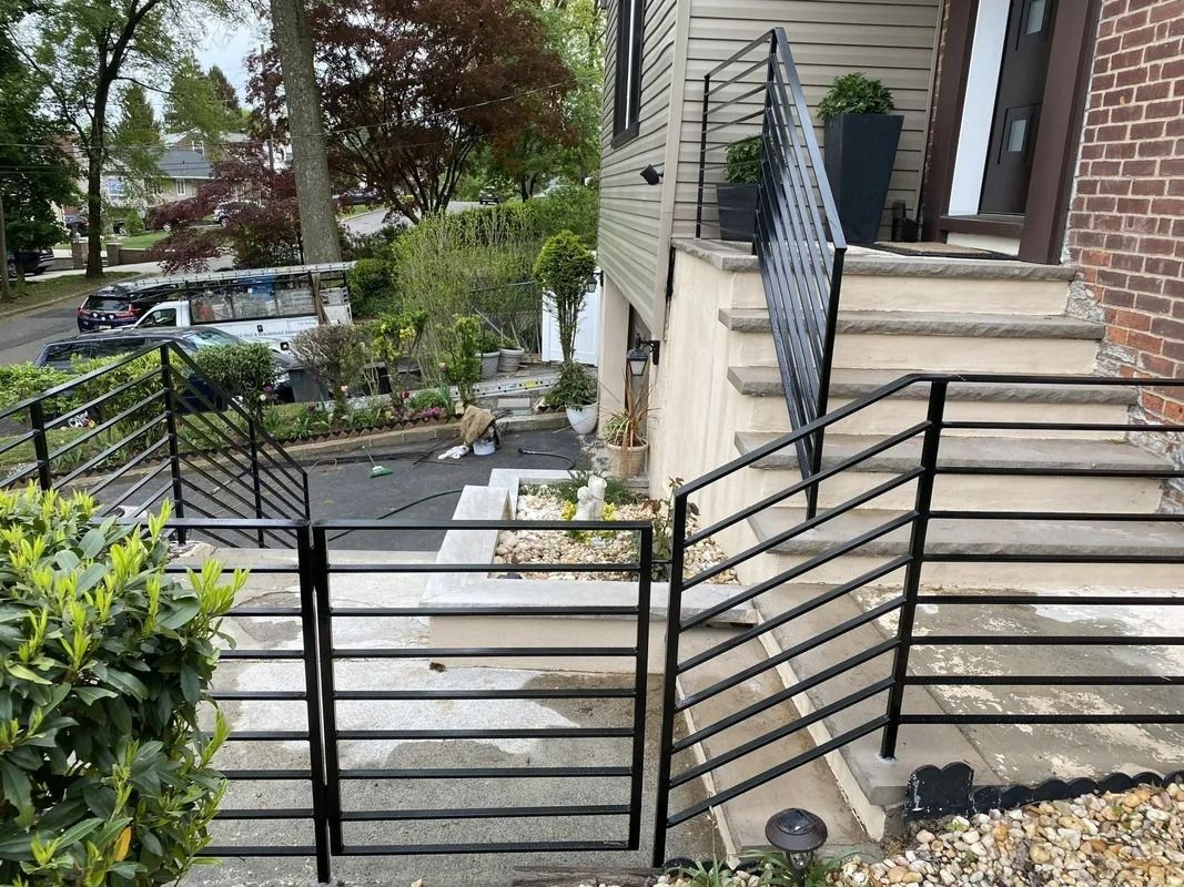 Black metal gate and railings lead up concrete steps to a house with beige siding and brick.
