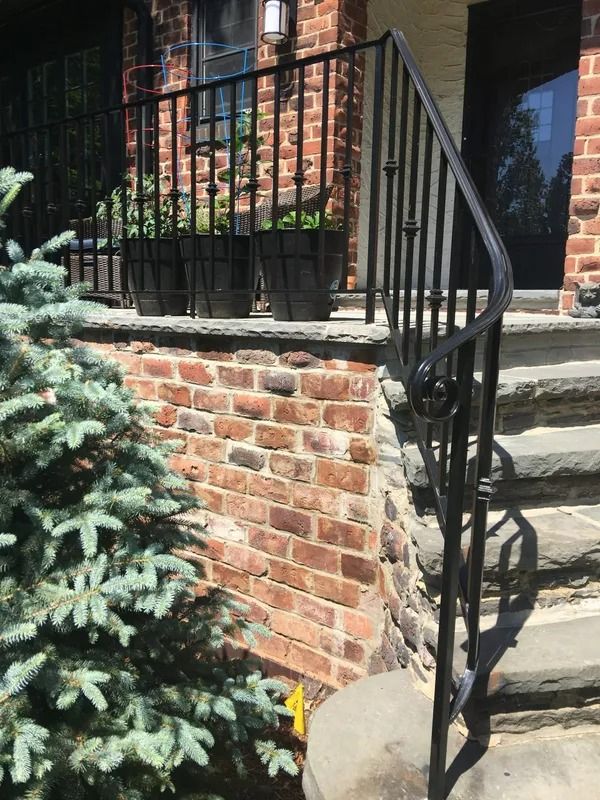 Black wrought-iron railing alongside brick and stone steps leading to a building with potted plants.
