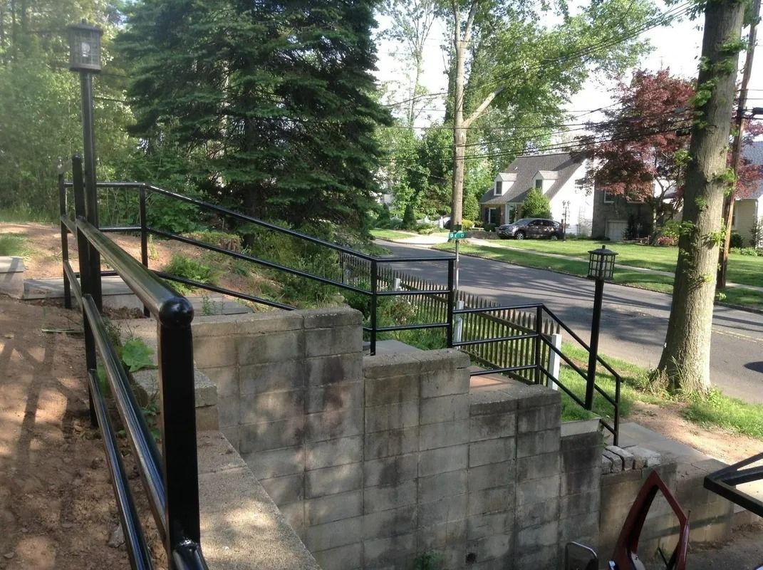 Staircase with black metal handrails leading up to a residential street with houses and trees.