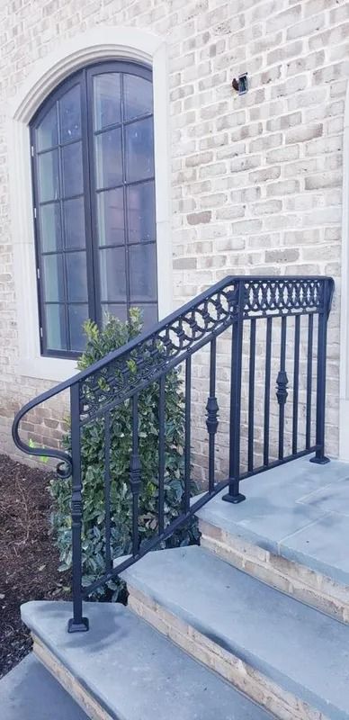 Black wrought iron railing on stone steps next to a brick wall and arched window.