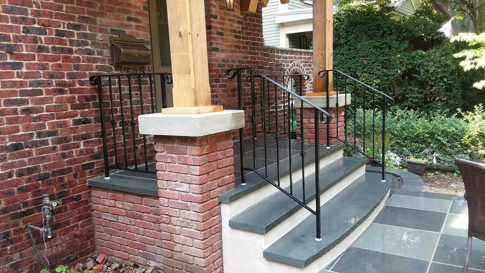 Brick porch with steps and black metal railings leading to a home entrance.