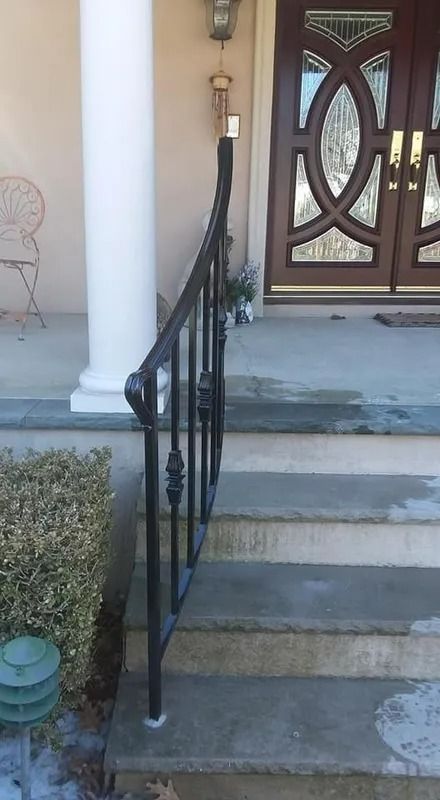 Black wrought-iron railing curves down concrete steps leading to a front door.