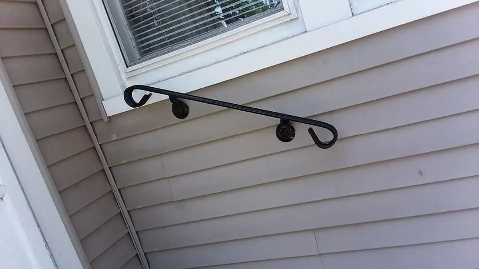 Black metal handrail attached to a beige, clapboard-sided building near a window.
