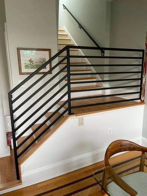 Black metal railing on a wooden staircase. Light wood floors, white walls, and artwork.