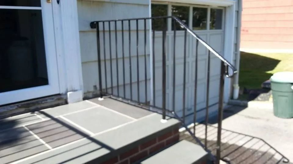 Black metal railing on a gray stone step leading to a door and garage.