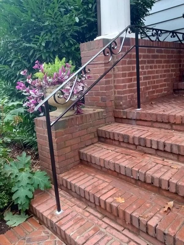 Brick steps with black wrought iron railing leading to a home's entrance, with a flower pot on a landing.