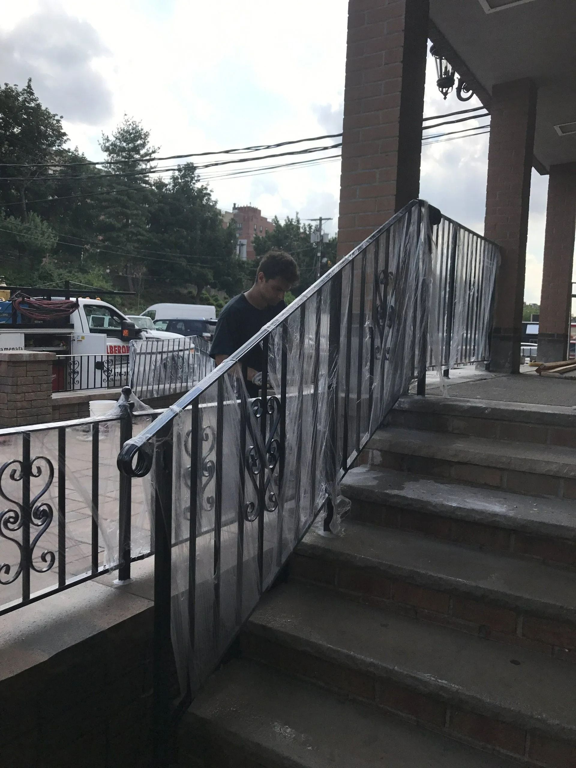 Person standing on stairs next to a metal railing covered in plastic, in front of a building.
