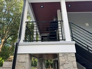 Covered porch with black railings and stairs on a house supported by stone pillars