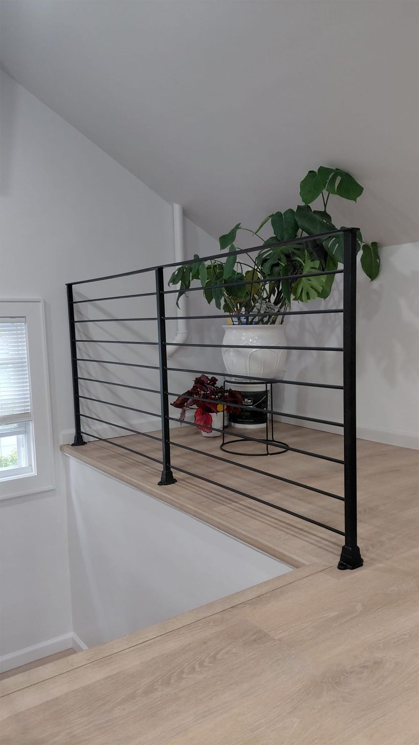Black metal stair railing with a potted hanging plant on a light wood loft landing.