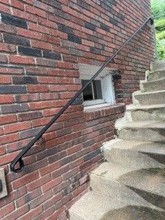 Brick exterior wall with a black handrail beside concrete steps and a small window.
