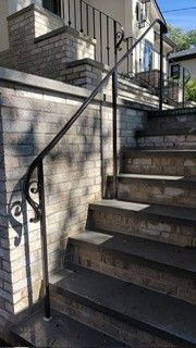Brick outdoor staircase with black metal handrail beside a house entrance