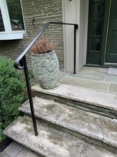 Front steps with black metal handrails beside a green door, and a potted plant on the landing.