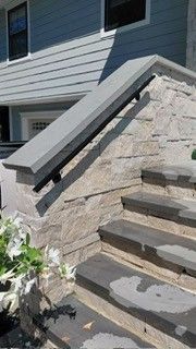 Stone staircase with gray handrail beside a house exterior and stone retaining wall