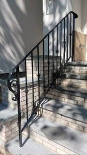 Black metal handrail beside sunlit outdoor concrete steps and beige wall
