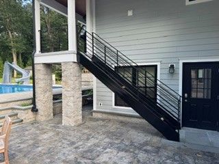 Covered patio with stone columns, black staircase, and gray house exterior.