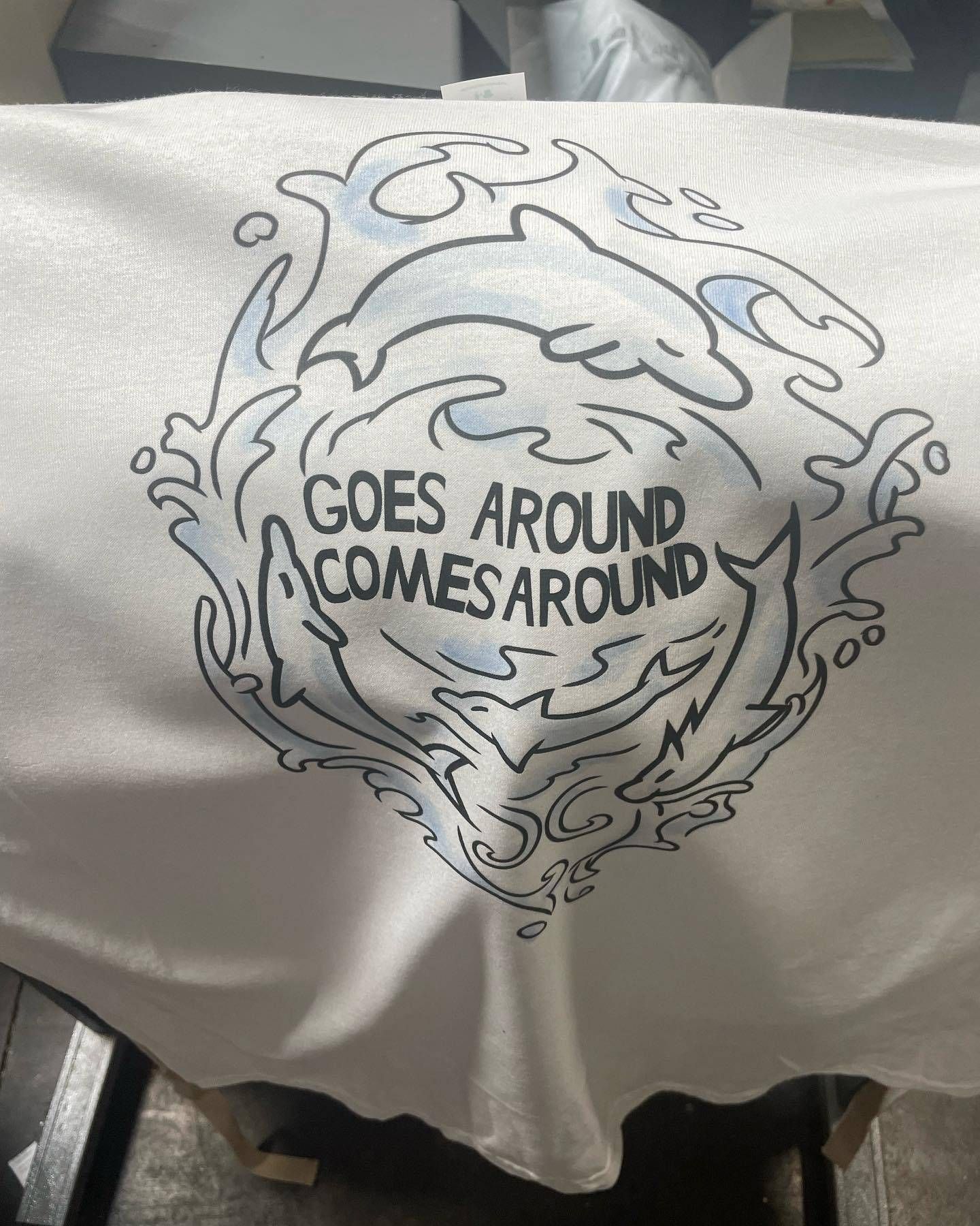 A white shirt with a drawing of a dolphin and the words `` goes around comes around ''