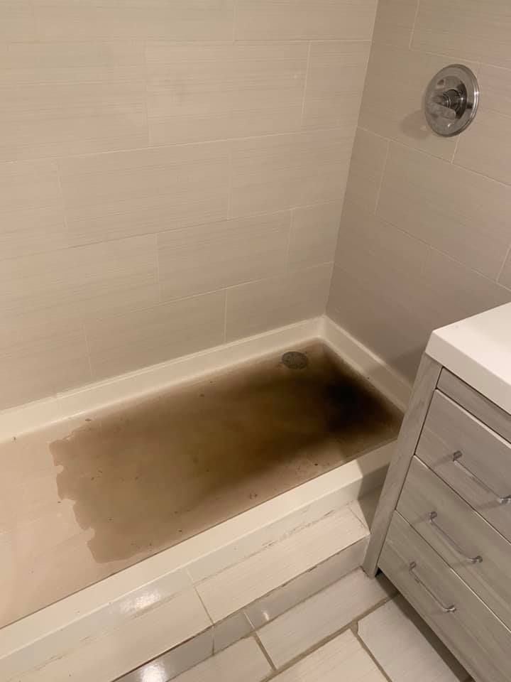 Dirty shower basin with brown stains; a white vanity is beside it.