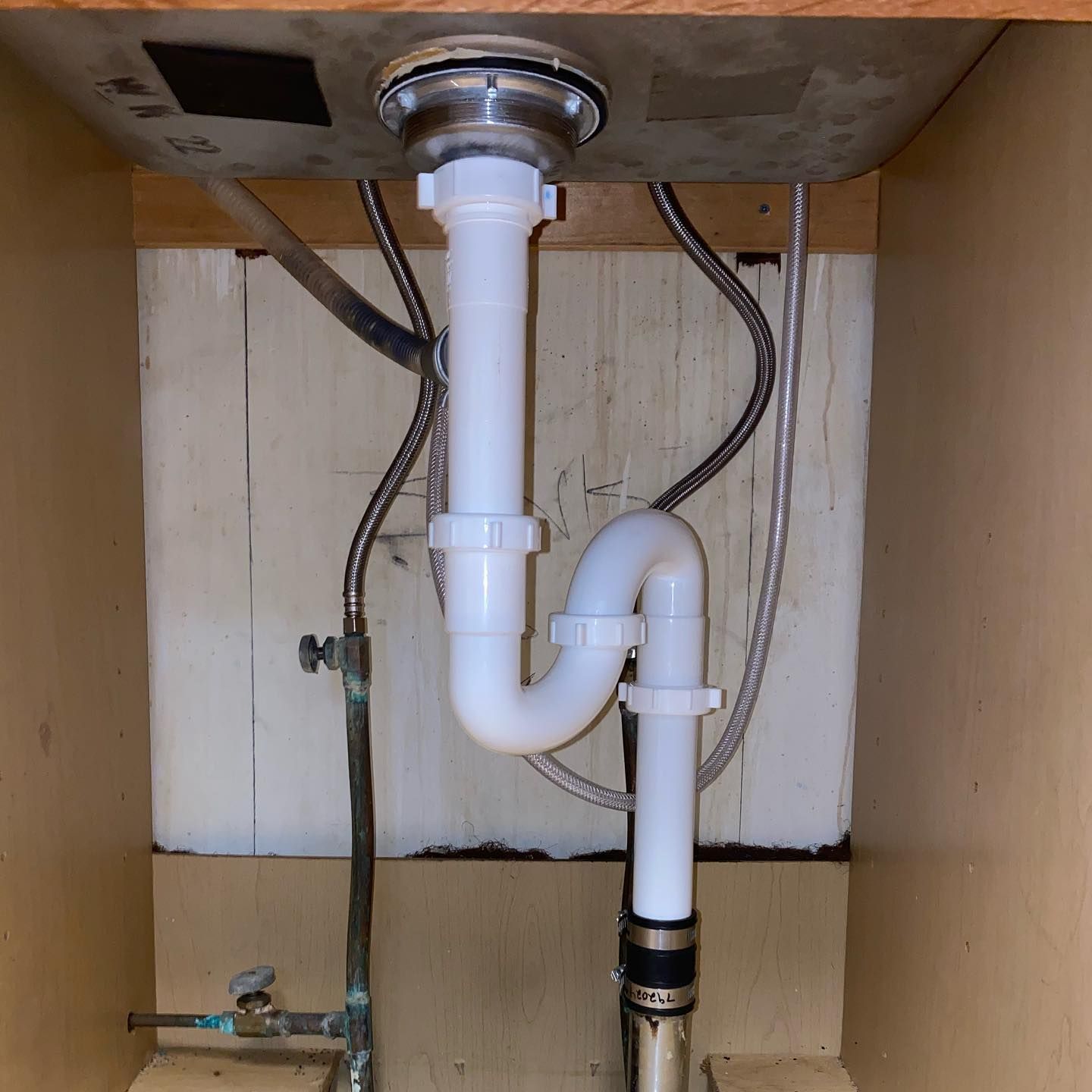 Under-sink plumbing: white plastic P-trap, drain pipes, and water supply lines inside a wooden cabinet.