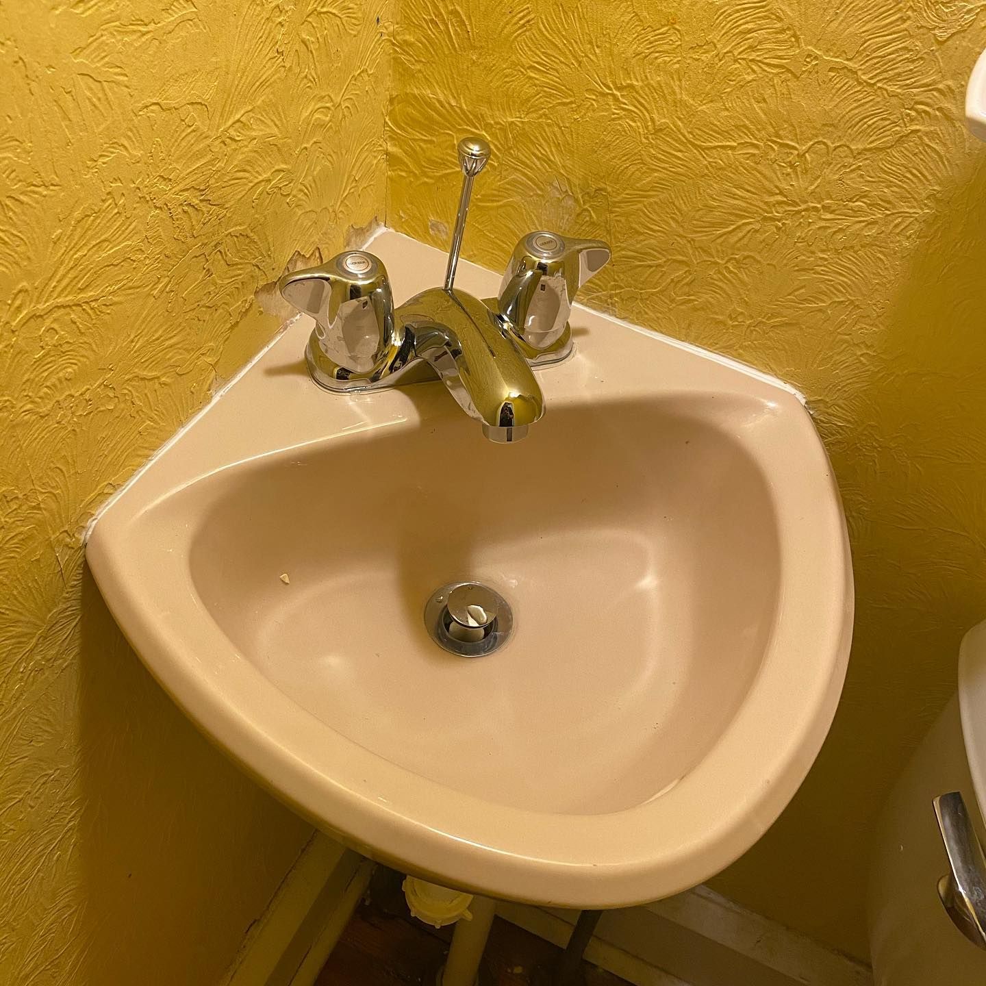 Pink corner sink with silver faucet against yellow textured wall.