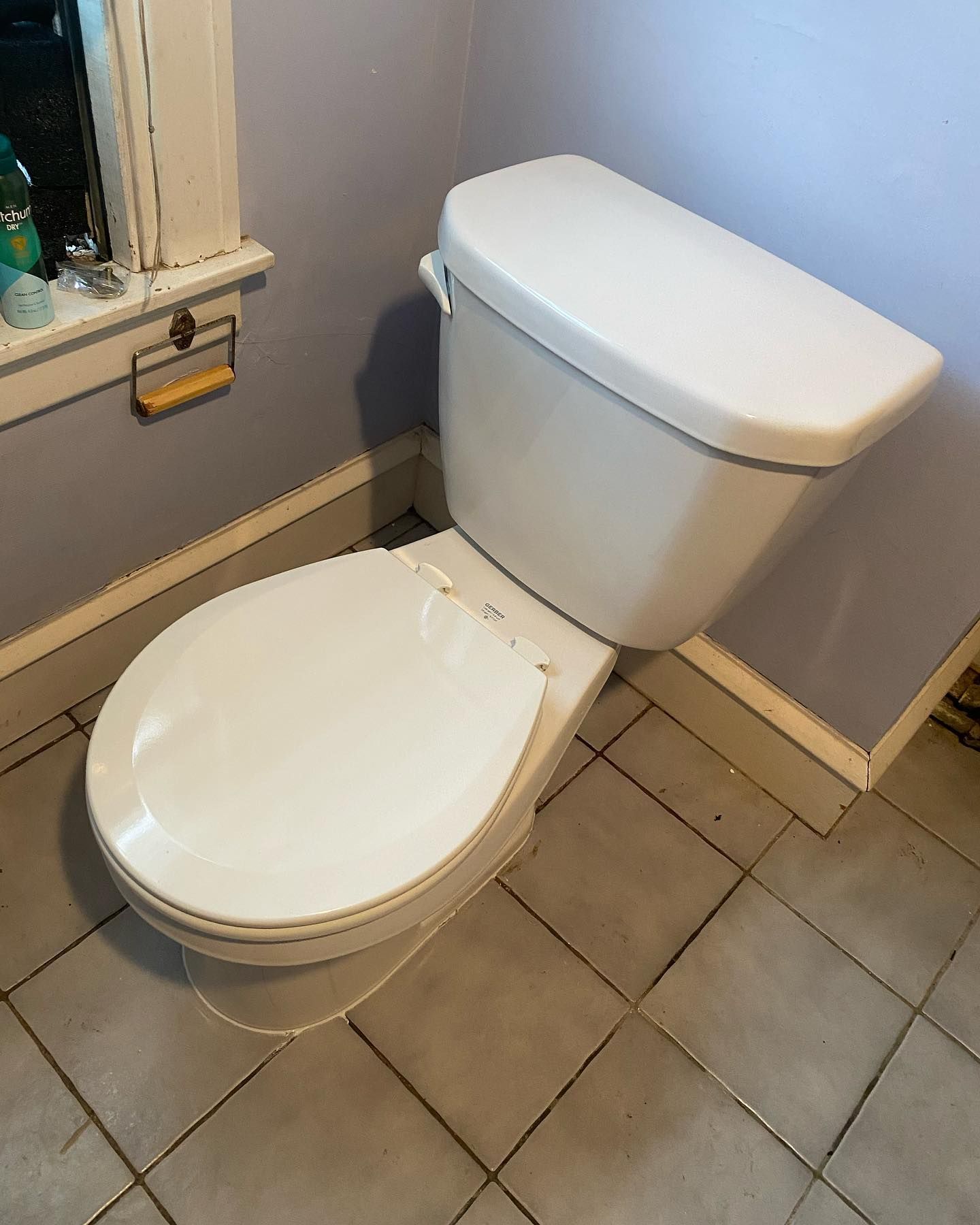 Toilet in a bathroom. White toilet and lid, beige tank, gray tiled floor, and pale blue walls.