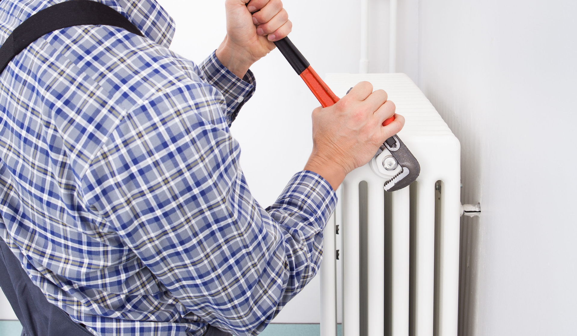 Man in plaid shirt using a wrench on a white radiator.