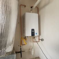White wall-mounted water heater with copper pipes and a black cable in a utility corner