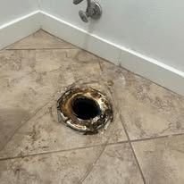 Bathroom floor with a broken, corroded drain opening in beige tile flooring