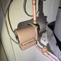 Brown utility meter mounted on a wall with copper pipes and a small flashlight illuminating it