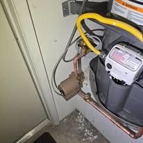 Water heater with yellow gas line and copper piping in a utility closet.