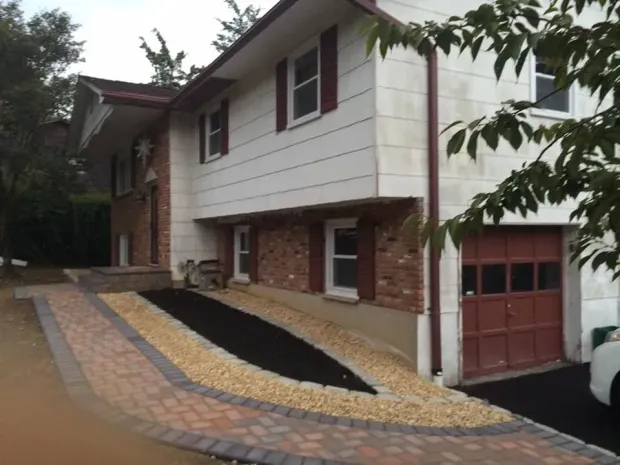 Two-story house with brick accents, driveway, and landscaping. Red garage door and brick walkway.