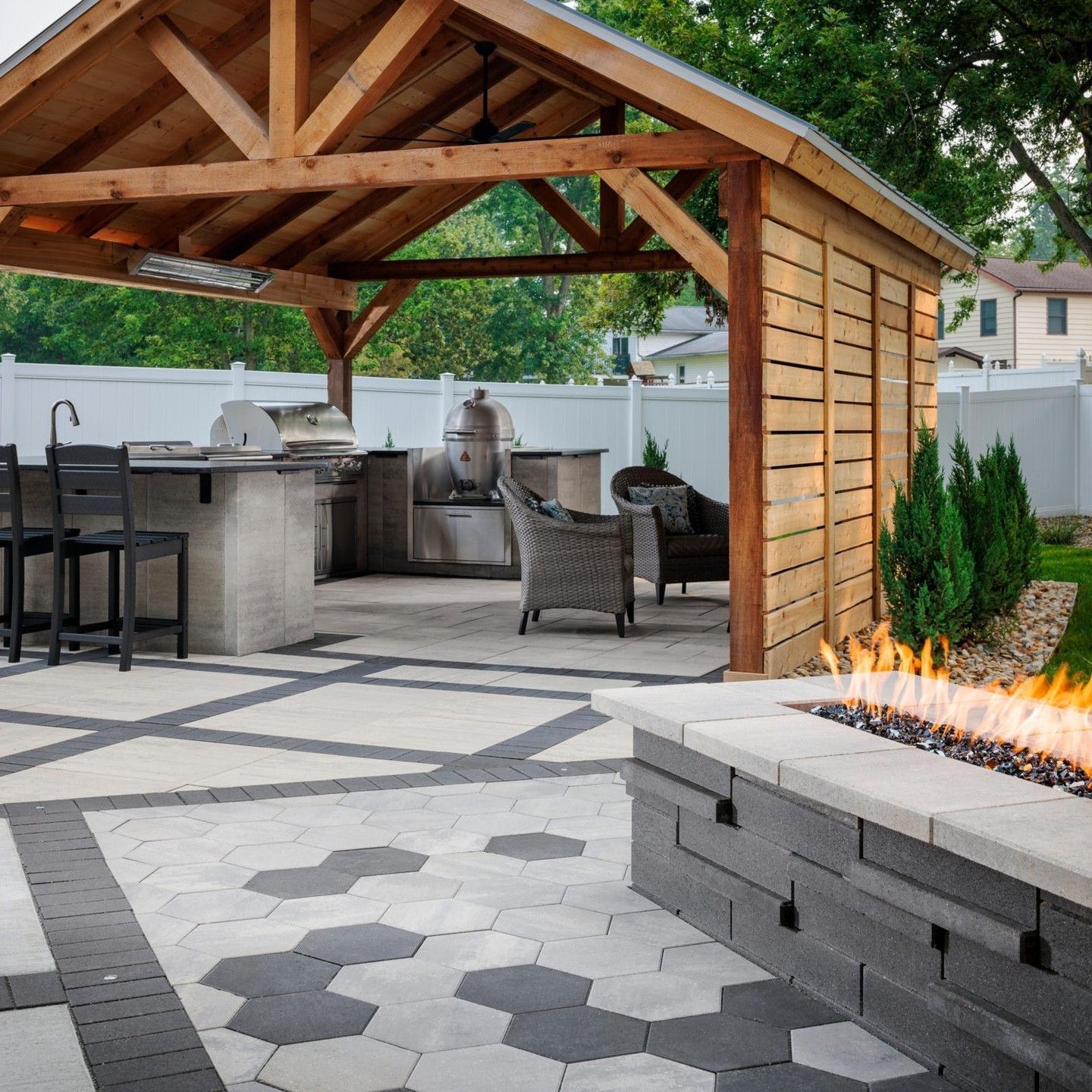 Outdoor kitchen with patio, fire pit, and wooden arbor. Stone and wood, neutral colors.