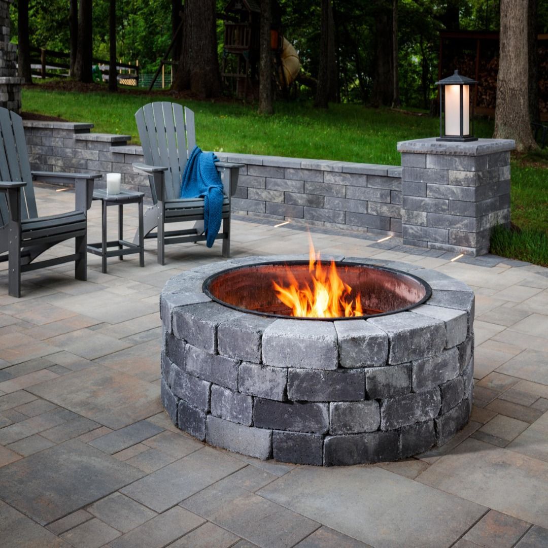 Fire pit with flames surrounded by stone, chairs, and a small table on a patio.