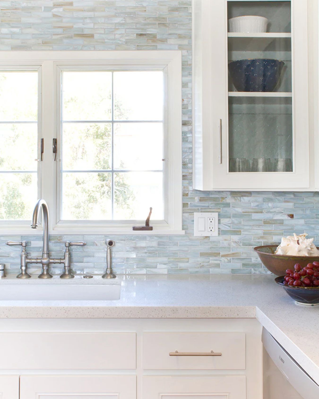 White kitchen with a light blue tile backsplash, a window above the sink, and a cabinet with glass doors.
